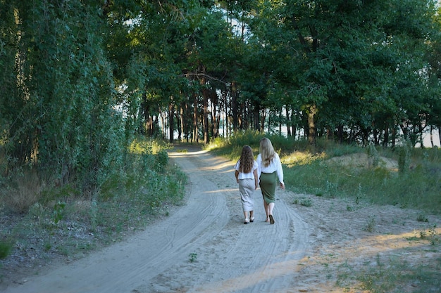 Dwie siostry trzymają się za ręce, idą ścieżką w dal