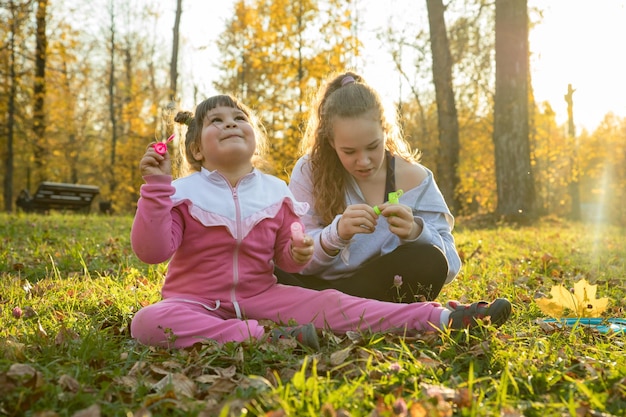 Dwie siostry w jesiennym parku mała dziewczynka siedząca na ziemi i kolejna siedząca obok niej