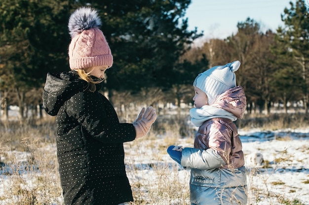 Dwie siostry w różnym wieku na zimowym spacerze w zaśnieżonym parku