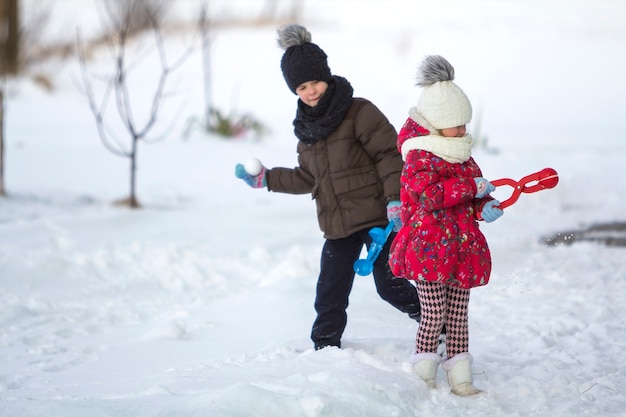 Dwie śliczne małe dzieci w ciepłych ubraniach z jasnymi klipami śniegu, grając, bawiąc się, robiąc śnieżki w zimowy zimny dzień na białym jasnym tle niewyraźne kopii. Aktywność na świeżym powietrzu, zabawy wakacyjne.