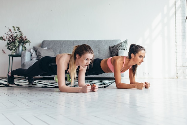 Dwie sprawne kobiety robią ćwiczenia deski na podłodze w domu Trening mięśni pleców i prasy, sport, trening fitness.