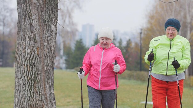 Zdjęcie dwie starsze kobiety w jesiennym parku mają nowoczesny zdrowy trening nordic walking