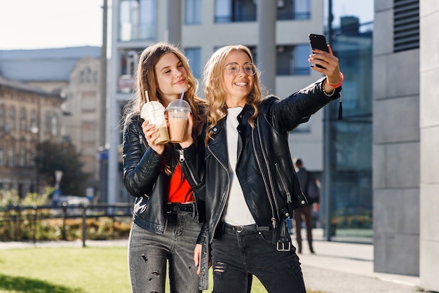 Dwie Stylowe Atrakcyjne Nastoletnie Dziewczyny Z Smoothie I Smartfonem Robiącym Selfie. Spędzanie Wolnego Czasu Z Najlepszymi Przyjaciółmi.