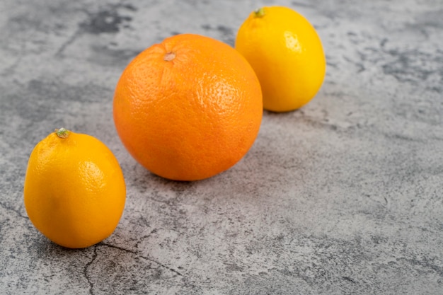 Dwie świeże Cytryny Ze Zdrową Pomarańczą Odizolowane Na Kamiennym Stole.