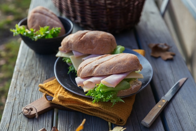 Zdjęcie dwie świeże kanapki z bagietką ciabatta z szynką, serem i sałatą na rustykalnym drewnianym tle