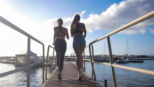 Dwie sylwetki młodych wysportowanych kobiet biegnących wzdłuż drogi wodnej
