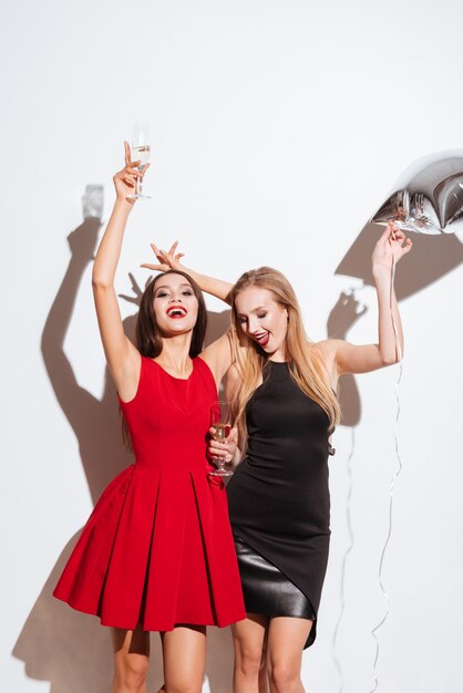 Dwie szczęśliwe atrakcyjne młode kobiety pijące szampana i imprezujące na białym tle