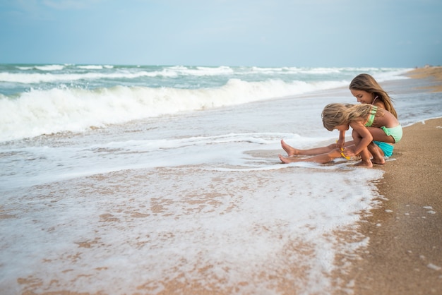 Dwie szczęśliwe dziewczynki spędzają wakacje na piaszczystej plaży lub podziwiają morskie fale w słoneczny letni dzień podczas wakacji. Koncepcja wakacji z dziećmi