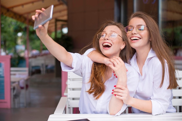 Dwie szczęśliwe dziewczyny robiące selfie w letniej kawiarni
