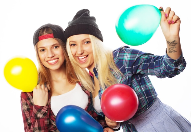 Dwie szczęśliwe hipsterki uśmiechające się i trzymające kolorowe balony na białym tle