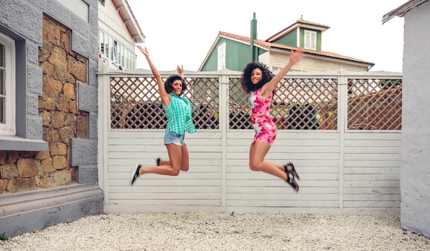 Dwie szczęśliwe młode kobiety skaczące przed białym ogrodzeniem