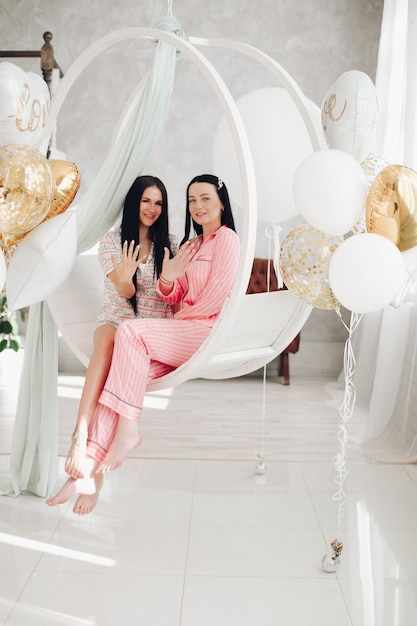 Dwie szczęśliwe przyjaciółki w piżamie siedzącej na stylowym fotelu w luksusowym wnętrzu