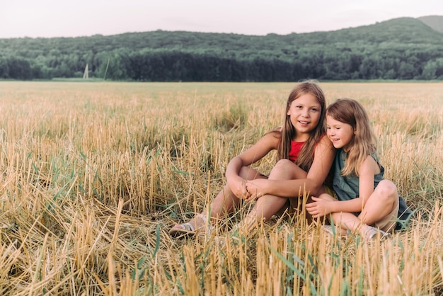 Dwie szczęśliwe siostry siedzą na polu w sianie i przytulają się Wysokiej jakości zdjęcie