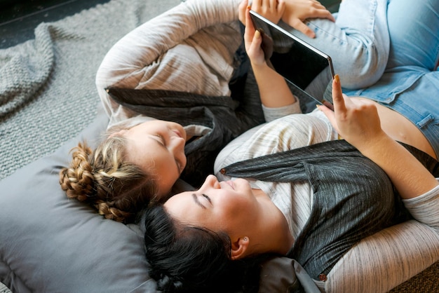 Zdjęcie dwie szczęśliwe siostry używają tabletu, leżąc na plecach na podłodze w domu