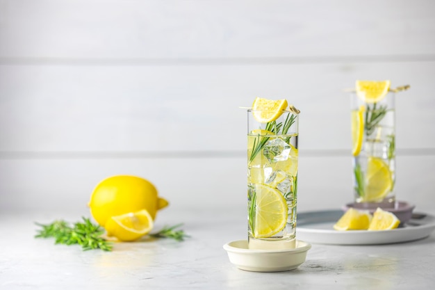 Dwie szklanki orzeźwiającego napoju cytrynowo-limonkowego z kostkami lodu w szklanych kielichach na jasnoszarym tle Letni świeży koktajl sodowy z rozmarynem