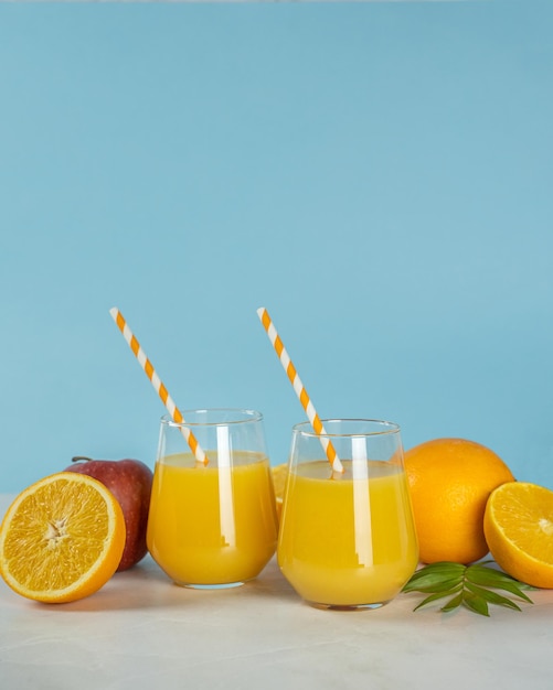 Dwie szklanki soku pomarańczowego z pomarańczami i słomką z zielonym liściem z boku.