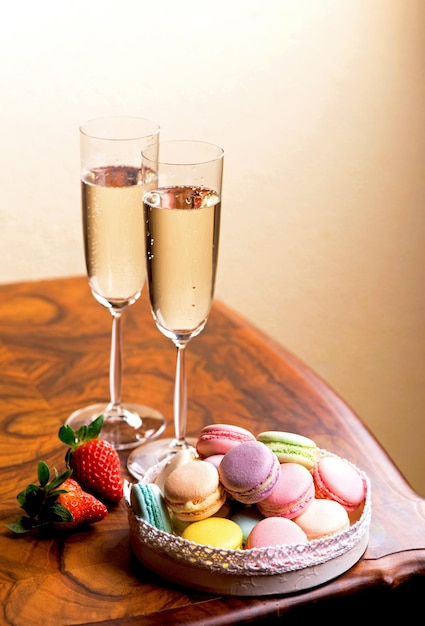 Dwie szklanki szampana i makaroniki z truskawkami na drewnianym stole