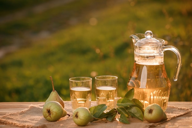 Dwie szklanki z sokiem gruszkowym i kosz z gruszkami na drewnianym stole z naturalnym tłem sadu na światło zachodzącego słońca Wegetariańska kompozycja owocowa