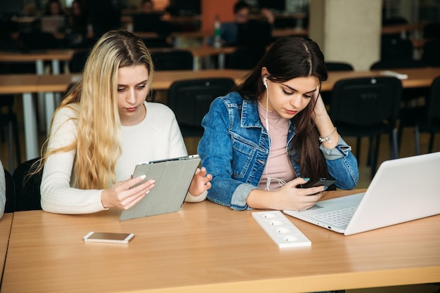 Dwie uczennice używają tabletu i laptopa w bibliotece i słuchają muzyki