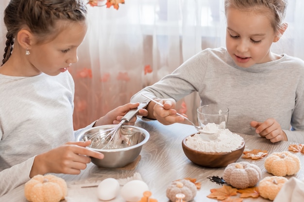 Dwie urocze dziewczyny biczują piernikowe ciasto, aby zrobić halloweenowe ciasteczka w domowej kuchni. Smakołyki i przygotowania do obchodów Halloween