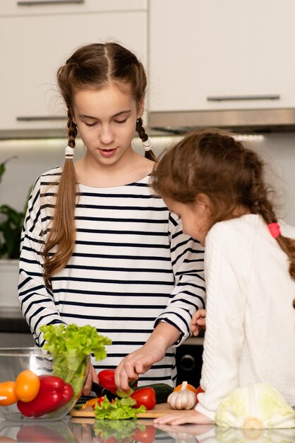 Dwie urocze siostry siostry kroją sałatkę ze świeżych warzyw. Zdrowe jedzenie. Dzieciństwo.