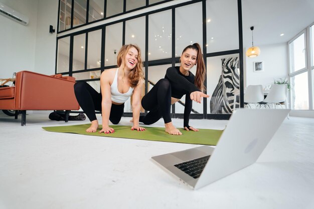 Dwie urocze sportowe kobiety wykonują ćwiczenia jogi w domu