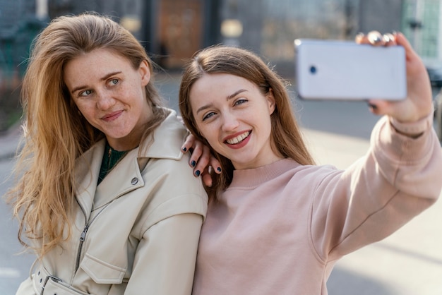 Zdjęcie dwie uśmiechnięte koleżanki na świeżym powietrzu w mieście przy selfie