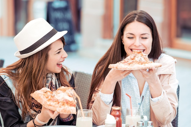 Dwie wesołe dziewczyny jedzące pizzę w kawiarni