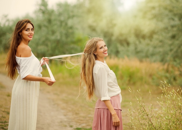 Dwie wesołe najlepsze dziewczyny w ubraniach w stylu retro na lądowaniu przy drodze w letni dzień