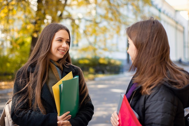 Dwie wesołe studentki rozmawiają w kampusie uniwersyteckim w słoneczny jesienny poranek