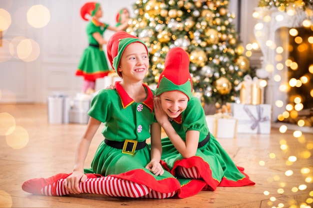 Dwie wesołe szczęśliwe dziewczyny w strojach elfów Świętego Mikołaja na tle choinki i innych dzieci