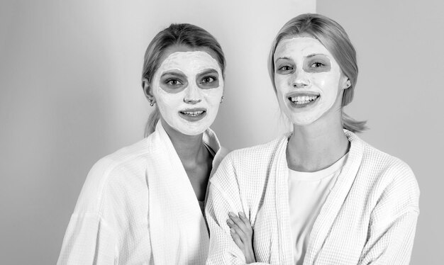 Zdjęcie dwie wesołe uśmiechnięte blondynki z naturalną maską na twarzy nad pięknym skincarem w tle