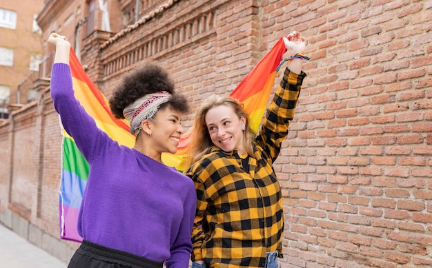 Zdjęcie dwie wielorasowe kobiety z flagą dumy gejowskiej na ulicy