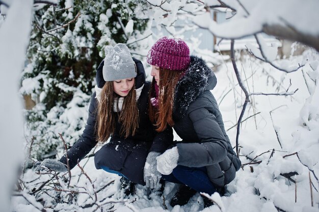 Dwie zabawne przyjaciółki bawią się w zimowy śnieżny dzień w pobliżu pokrytych śniegiem drzew
