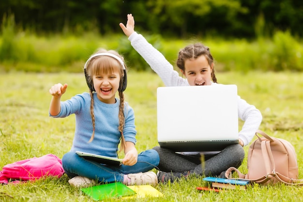 Zdjęcie dwie zabawne uczennice siedzą na trawie i czytają książki. dziewczyny, dziewczyny, siostry uczą się lekcji przyrody.