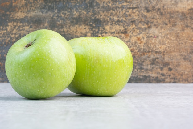 Dwie zielone dojrzałe jabłka na marmurze.