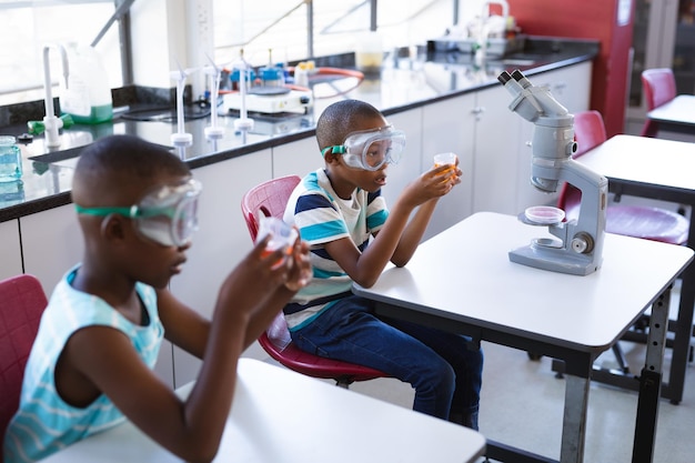 Dwóch afrykańskich chłopców w okularach ochronnych trzymających zlewkę w klasie naukowej w laboratorium