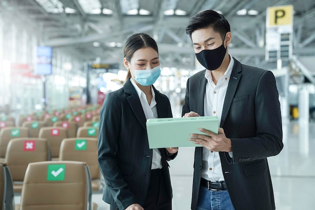 Dwóch azjatyckich biznesmenów i bizneswoman z maską na twarz w międzynarodowym terminalu na lotnisku rozmowa na temat spotkania w pobliżu ławki w pobliżu nowej normalnej koncepcji biznesowej podróży