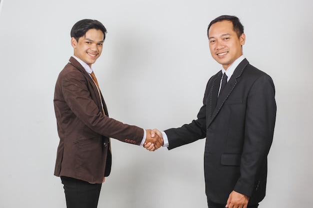 Dwóch azjatyckich biznesmenów w garniturze i krawacie patrzących w kamerę podczas wspólnego uścisku dłoni