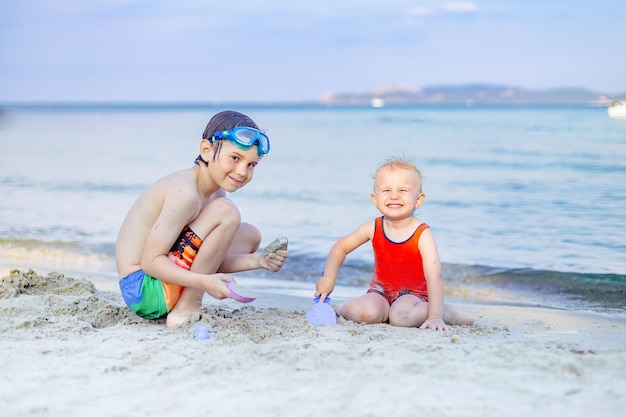 Dwóch braci bawiących się na piasku nad morzem. Zajęcia na plaży dla dzieci na świeżym powietrzu latem. Szczęśliwe rodzinne wakacje koncepcja, skopiuj spację.