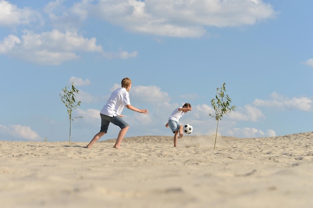 Dwóch braci grających w piłkę nożną na plaży w letni dzień