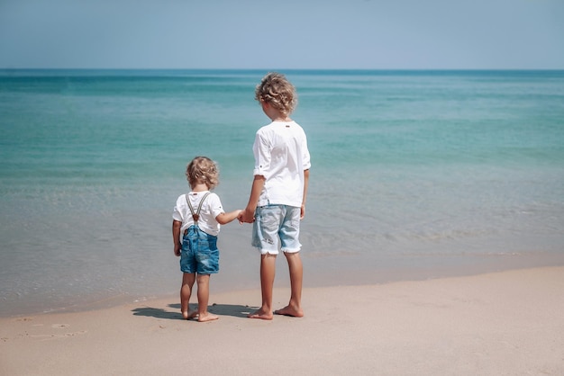 Dwóch braci relaks na plaży nad morzem. Mały chłopiec trzyma rękę swojego starszego brata.