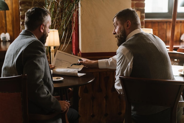 Dwóch brodatych mężczyzn w staromodnych garniturach rozmawia lub rozmawia o czymś w restauracji