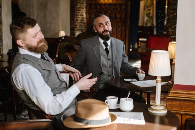 Dwóch brodatych mężczyzn w staromodnych garniturach rozmawia lub rozmawia o czymś w restauracji