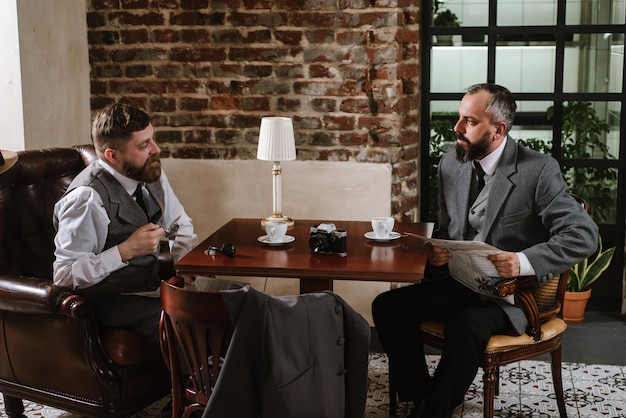 Zdjęcie dwóch brodatych mężczyzn w staromodnych garniturach rozmawia lub rozmawia o czymś w restauracji