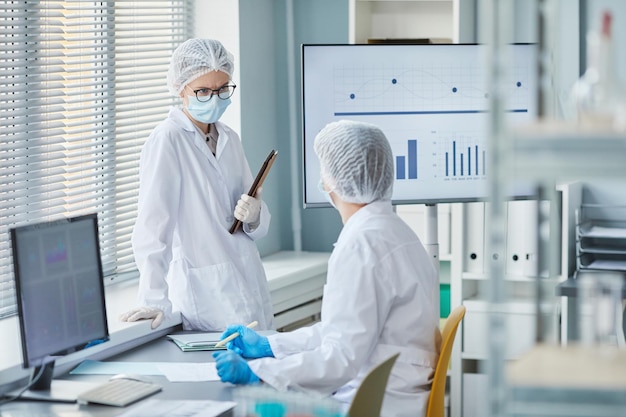 Dwóch chemików w fartuchach laboratoryjnych rozmawia ze sobą podczas pracy nad statystykami epidemii w laboratorium
