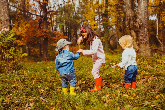 Dwóch chłopców i dziewczynka bawią się gałęziami w jesiennym parku