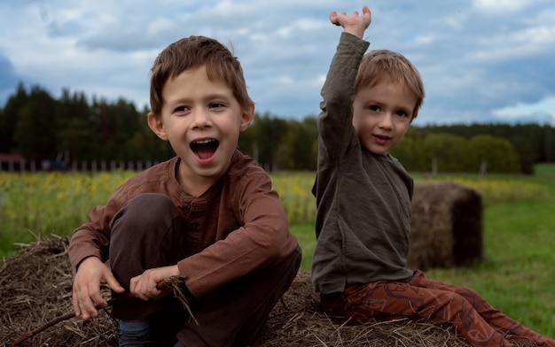 Zdjęcie dwóch chłopców siedzi na strychu. dwaj bracia uśmiechają się i śmieją, siedząc na stogu siana,