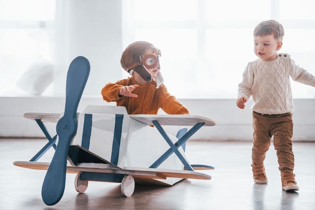 Dwóch chłopców w mundurach pilotów w stylu retro bawi się samolotem zabawkowym w pomieszczeniu