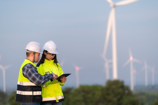 Zdjęcie dwóch inżynierów pracujących i trzymających raport na farmie turbiny wiatrowej power generator station na górze ludzie z tajlandii technik mężczyzna i kobieta rozmawiają o pracy